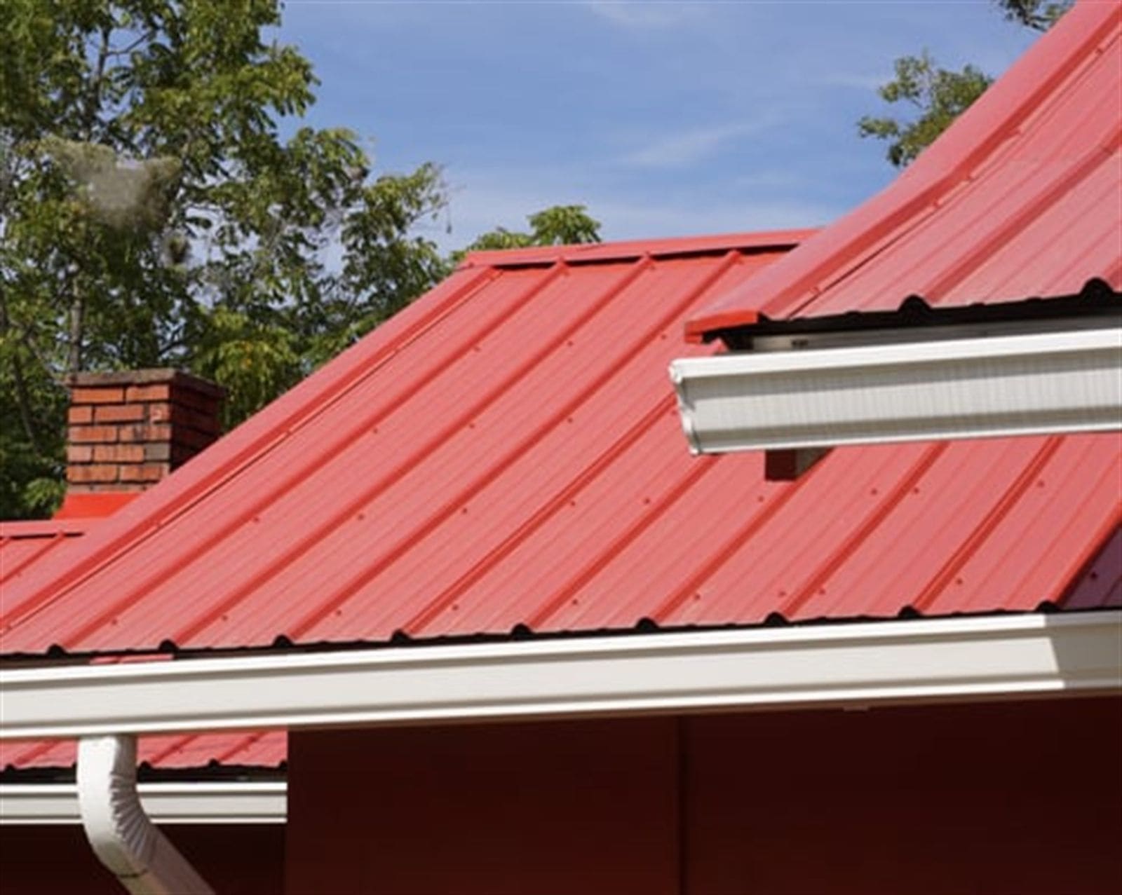 Newly installed white seamless gutter running along a red metal roofline